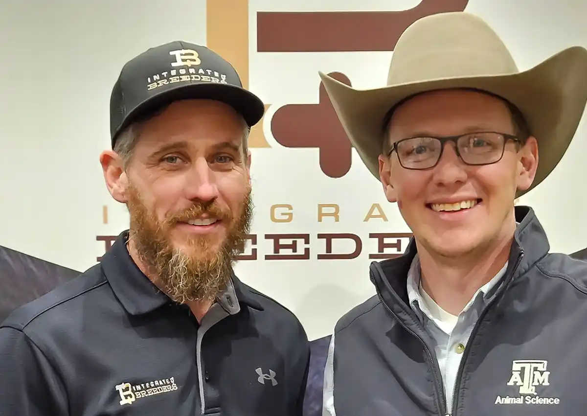 Drs. Cody and Ky Pohler stand smiling in front of the Integrated Breeders logo